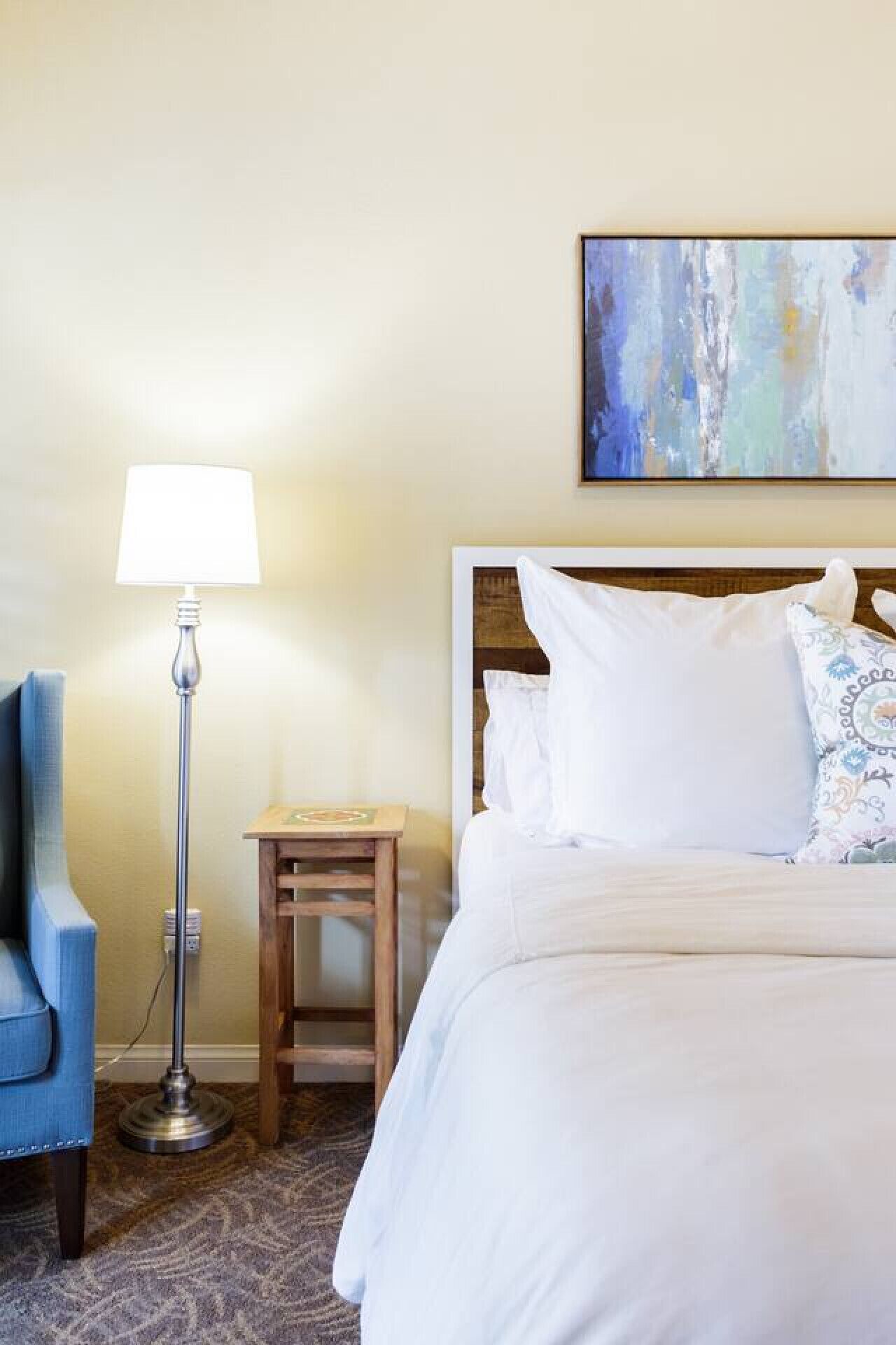 Een hotelkamer met een bed, nachtkastje, lamp en stoel.