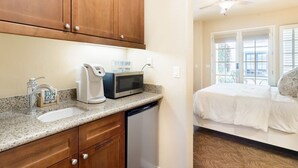 A kitchen with a microwave, coffee maker, and a sink. There is a bed with white bedding and a window with blinds. - Serene Studio in the Resort-Style Legacy Villas Complex (La Quinta)