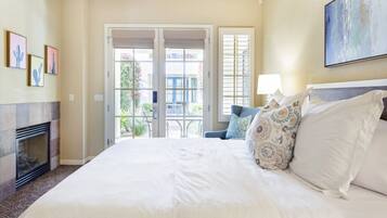 A hotel room with a large bed, a fireplace, a balcony with a view, and artwork on the walls.
