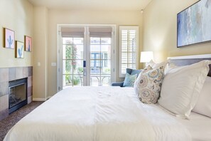 Une chambre d’hôtel avec un grand lit, une cheminée, un balcon avec vue et des œuvres d’art aux murs.
