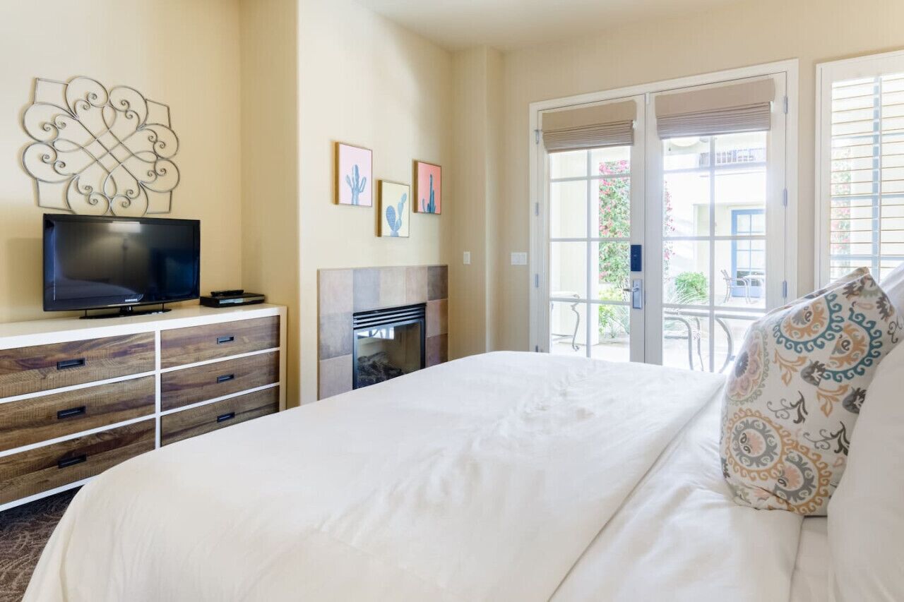 A hotel room with a bed, a television, a fireplace, and a balcony with a view of the outside.