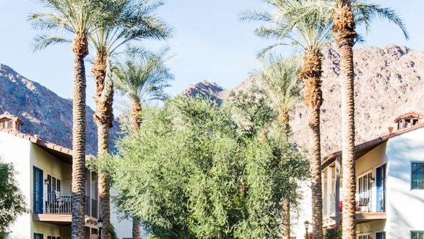 A swimming pool with a waterfall feature, surrounded by palm trees and a mountain backdrop. - Serene Studio in the Resort-Style Legacy Villas Complex (La Quinta)
