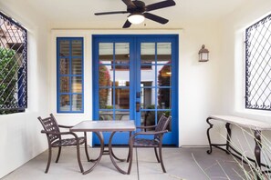 Une terrasse avec une table et des chaises, un ventilateur de plafond et une porte bleue avec des fenêtres.