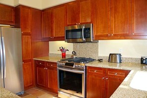 Une cuisine avec des meubles en bois, des appareils en acier inoxydable et des plans de travail en granit.
