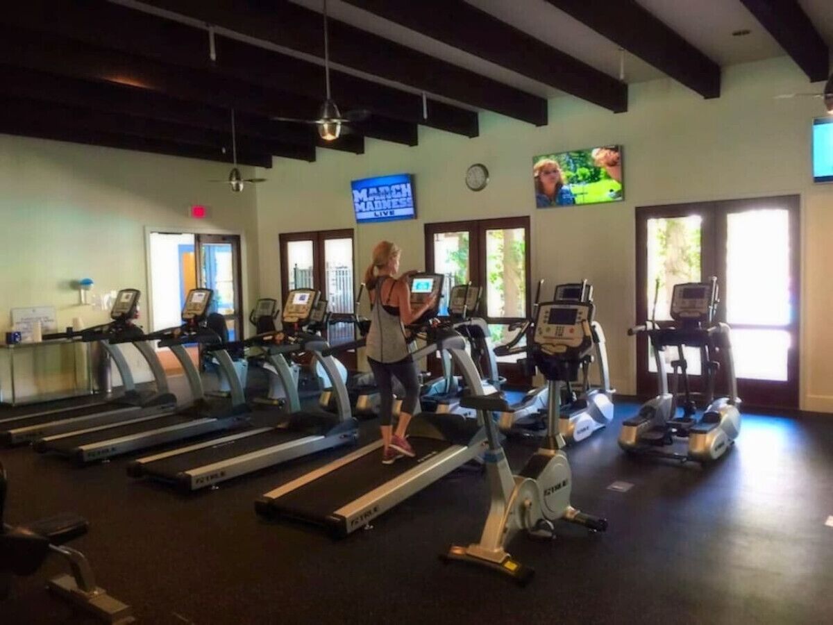 A gym with treadmills, ellipticals, and a woman using a treadmill.