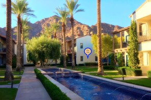 Un resort con piscina, palmeras y montañas al fondo.