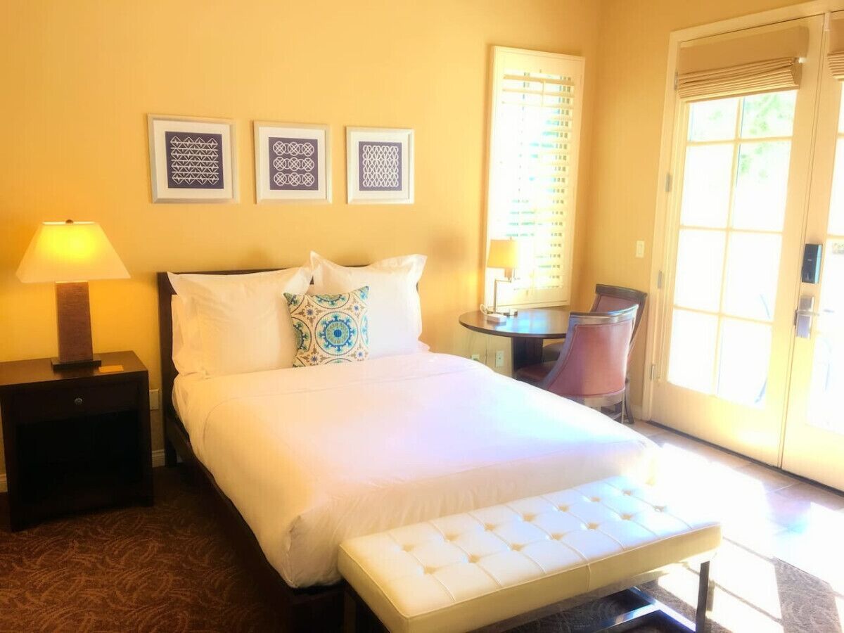 A hotel room with a bed, bedside tables, a chair, and a window with blinds.