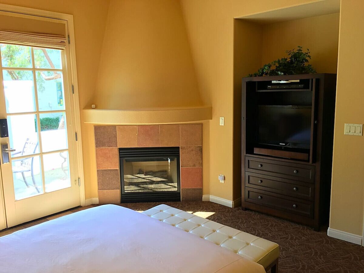 Un dormitorio con cama, chimenea, televisión y puerta que da a un espacio exterior.