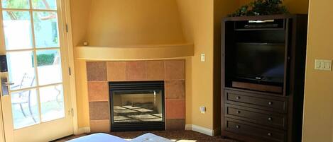 Un dormitorio con cama, chimenea, televisión y puerta que da a un espacio exterior.