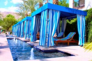 Zona de piscina con toldos azules y sillas de descanso.