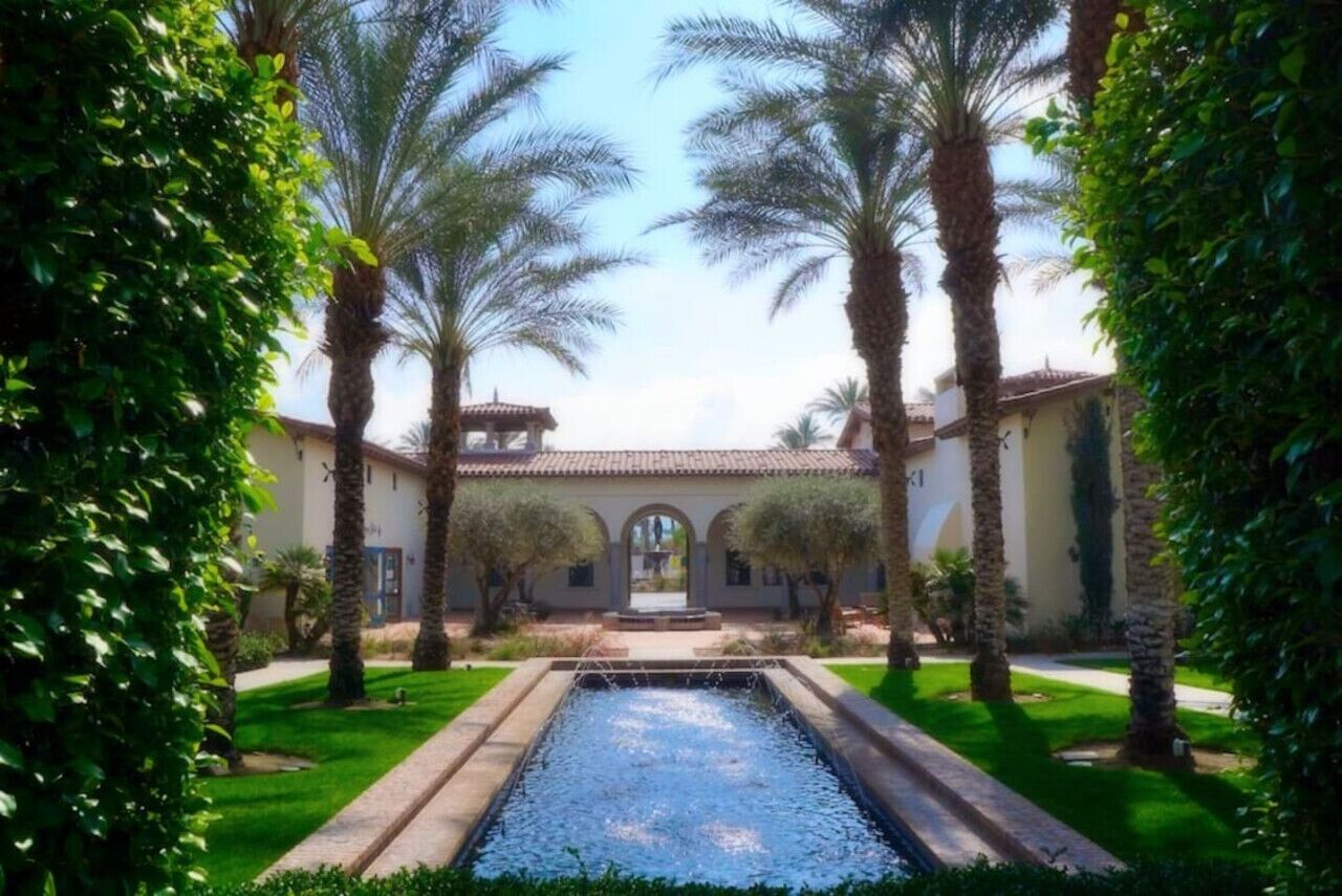 A courtyard with a water feature, palm trees, and a building with arches.
