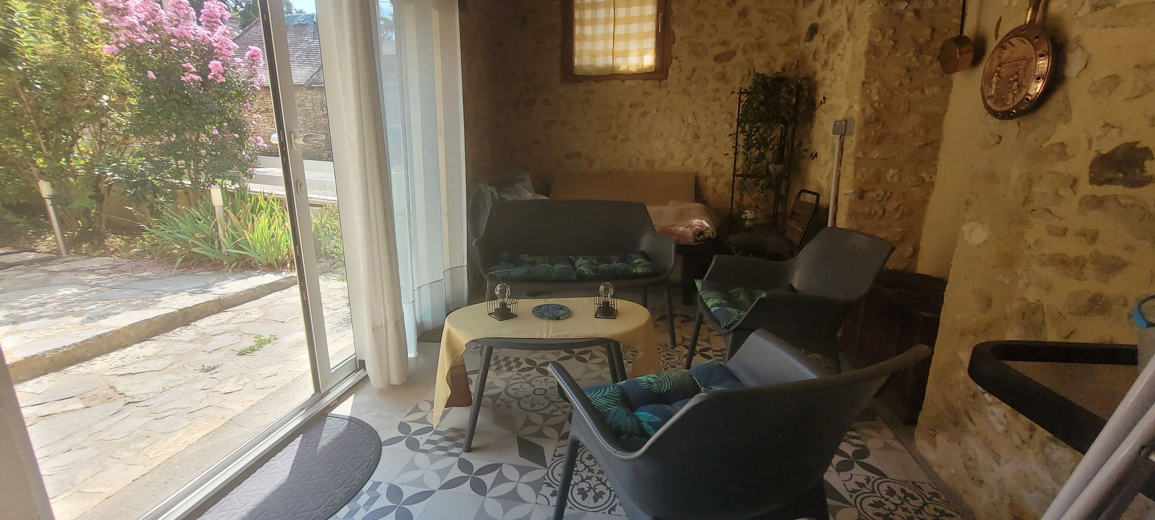 A room with a stone wall, a window with a view of greenery, a table with a chair, and a small decorative item on the wall.