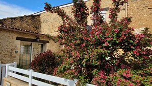 A stone building with a tiled roof, a white fence, and a flowering bush in front. - Charmant Gîte 3 Cosy, Climatisé, Environnement Bucolique, en Périgord Noir (Sagelat)