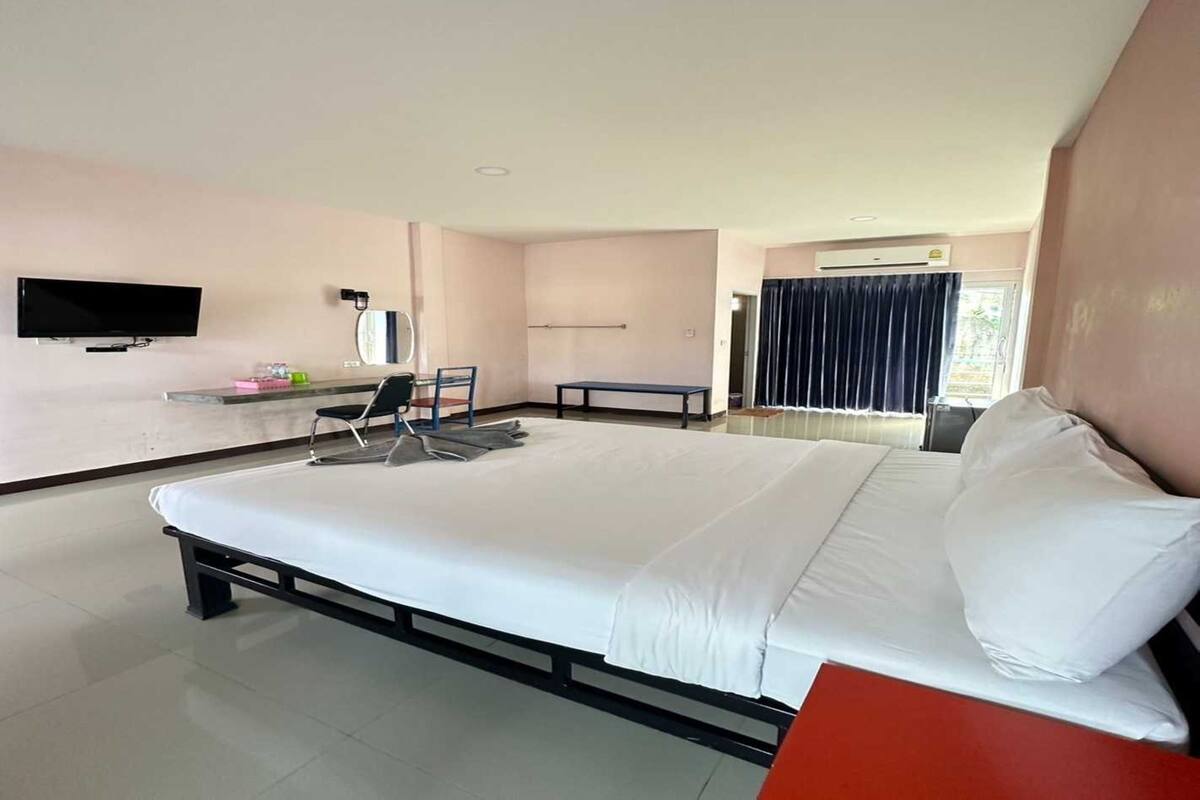 A modern hotel room with a large bed, a desk, a chair, a TV, and a window with curtains.
