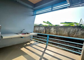 A balcony with a sink and a railing, overlooking a concrete wall and greenery. - OYO 75467 Baan Siripornchai 2 (Sakon Nakhon)