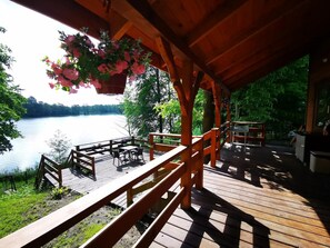 A wooden deck with outdoor seating overlooking a lake. - Domek uroczo położony we wsi Drynki, przy jeziorze Pozorty. Osada 4-ech domków (Maldyty)