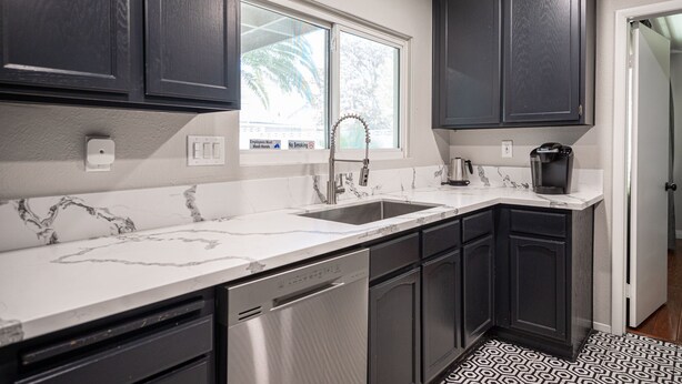 A kitchen with dark cabinets, a white marble countertop, a stainless steel sink, and a coffee maker.