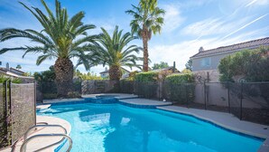 A swimming pool with a clear blue water, surrounded by palm trees and a fence.