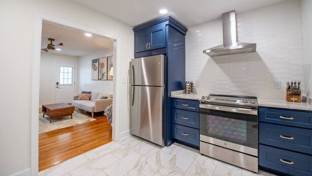 A modern kitchen with stainless steel appliances, blue cabinets, and a white tiled backsplash. - Cottage @ Midtown - Central Location! (Duplex) (Tallahassee)