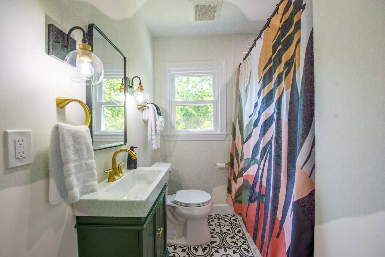 Een badkamer met een wit wastafel, een groene wastafelmeubel, een wit toilet en een douchegordijn met bladmotief.