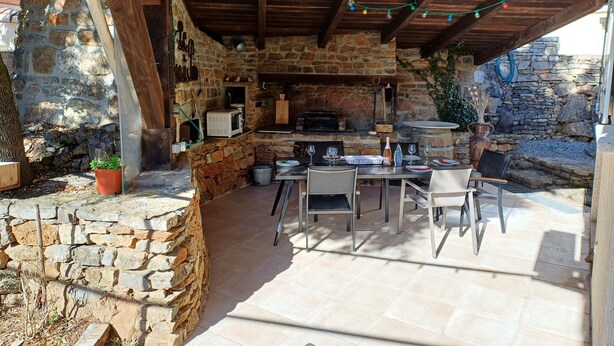 Une terrasse extérieure avec des murs en pierre, une pergola en bois et une cheminée en pierre.