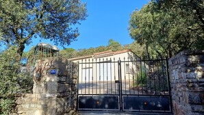 Une entrée fermée par un portail, donnant accès à un bâtiment doté d’un mur en pierre et d’un portail en métal, le tout entouré d’arbres.