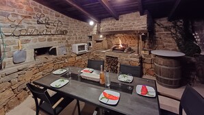 Un intérieur rustique en pierre, avec une cheminée en pierre, des poutres en bois et une table à manger dressée pour quatre personnes.