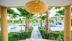 A poolside area with a pathway leading to a seating area, surrounded by palm trees and a decorative hanging light. - Luxury heated pool Villa Marrakech (Marrakech)
