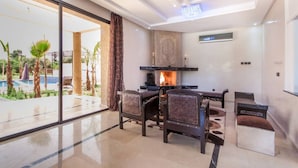 A modern living room with a fireplace, a glass door leading to a pool, and a view of palm trees. - Luxury heated pool Villa Marrakech (Marrakech)