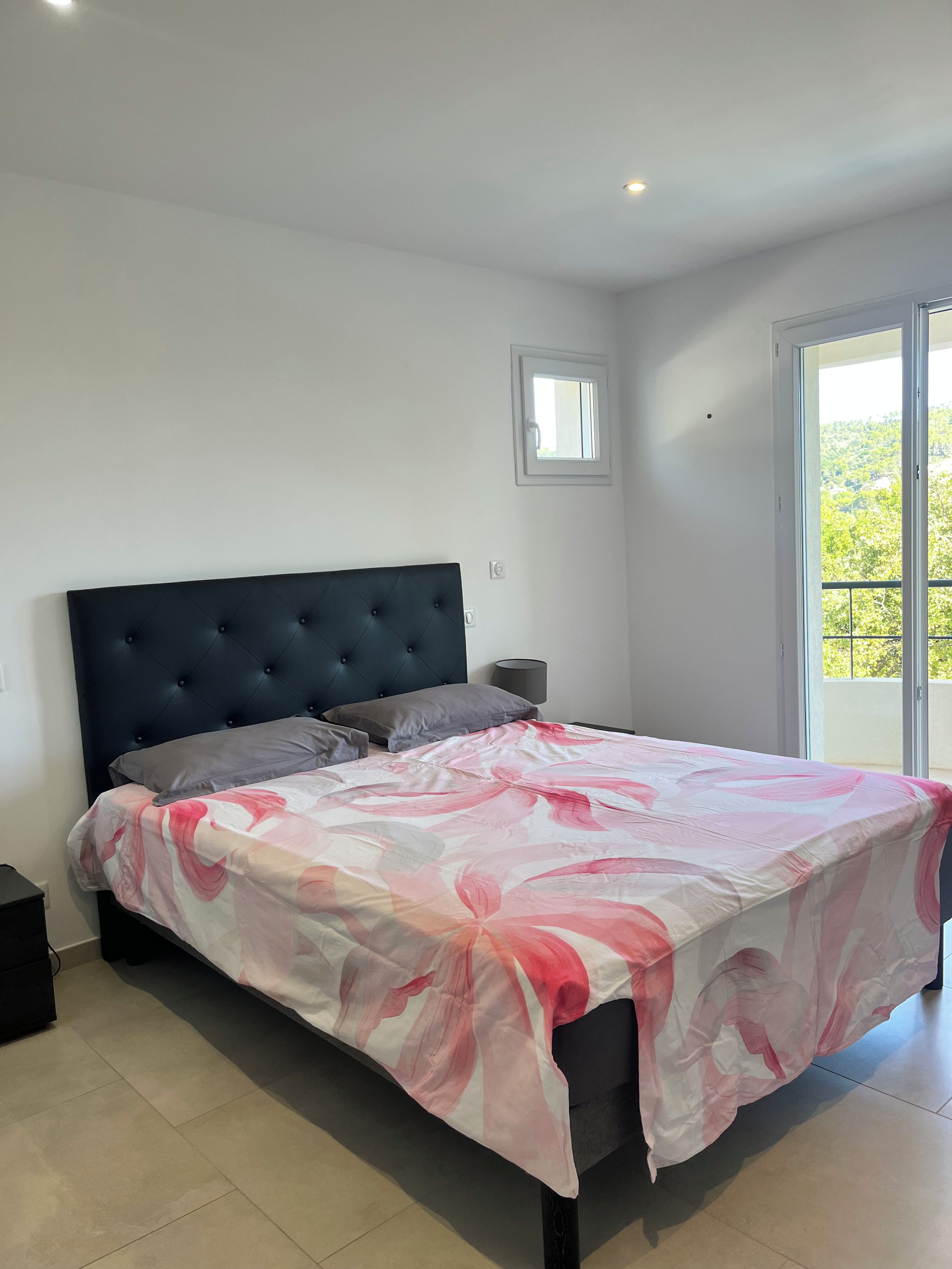 A bedroom with a bed, a nightstand, a window, and a door.