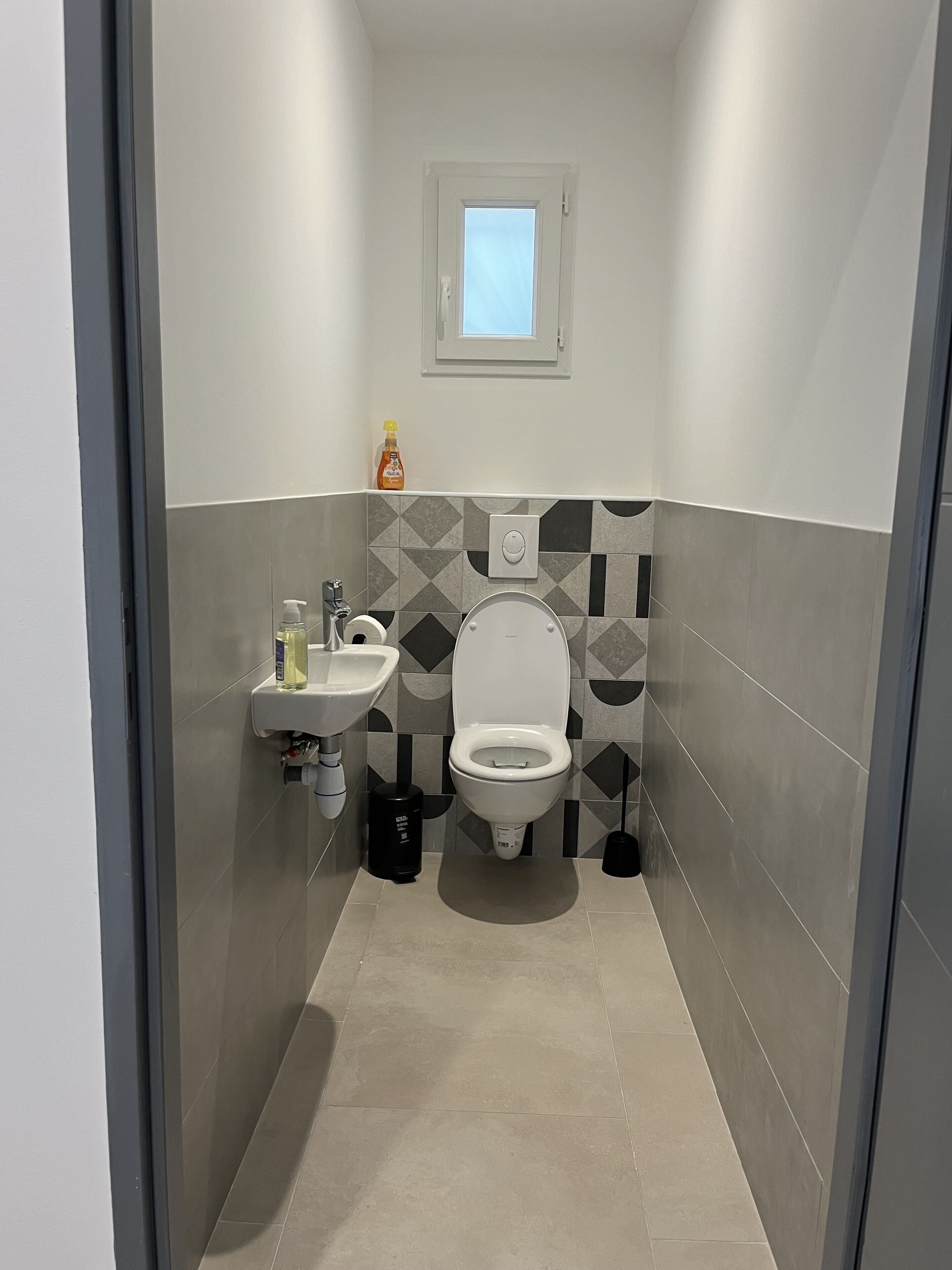 Un bagno stretto con il water, un lavandino e una finestra sopra il water.