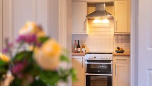 Une cuisine avec des meubles blancs, une cuisinière et un four. On aperçoit un vase rempli de fleurs au premier plan.