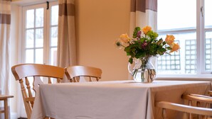 Un coin repas avec une table dressée pour deux personnes, des chaises en bois et un vase de fleurs posé sur la table.