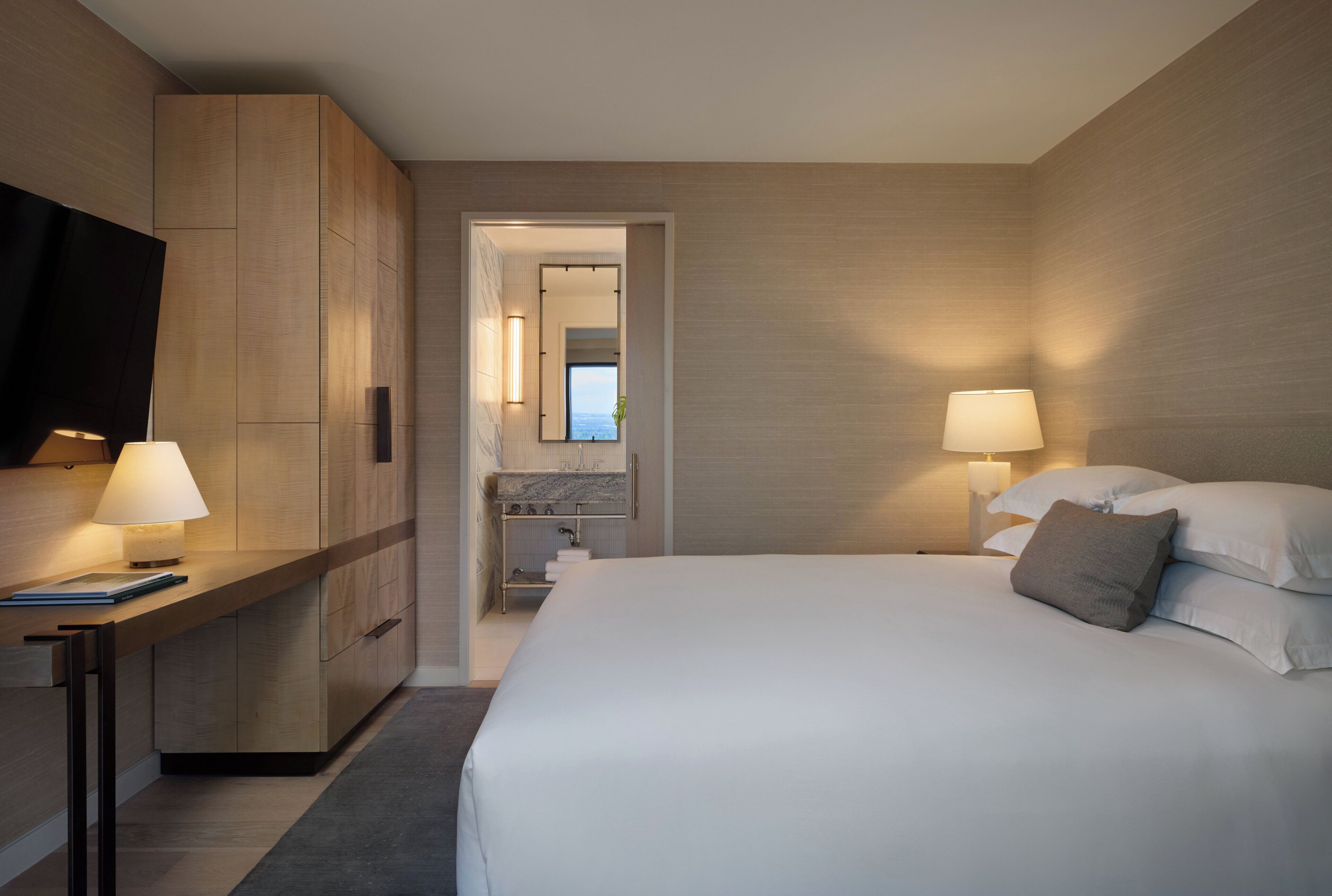 Une chambre d’hôtel moderne dotée d’un grand lit, de lampes de chevet, d’un téléviseur à écran plat et offrant une vue sur la mer par une fenêtre.