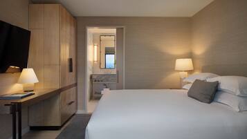 Une chambre d’hôtel moderne dotée d’un grand lit, de lampes de chevet, d’un téléviseur à écran plat et offrant une vue sur la mer par une fenêtre.
