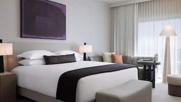 Ett modernt hotellrum med en stor säng, två sängbord, en soffa, ett litet bord med en lampa och ett stort fönster med gardiner.