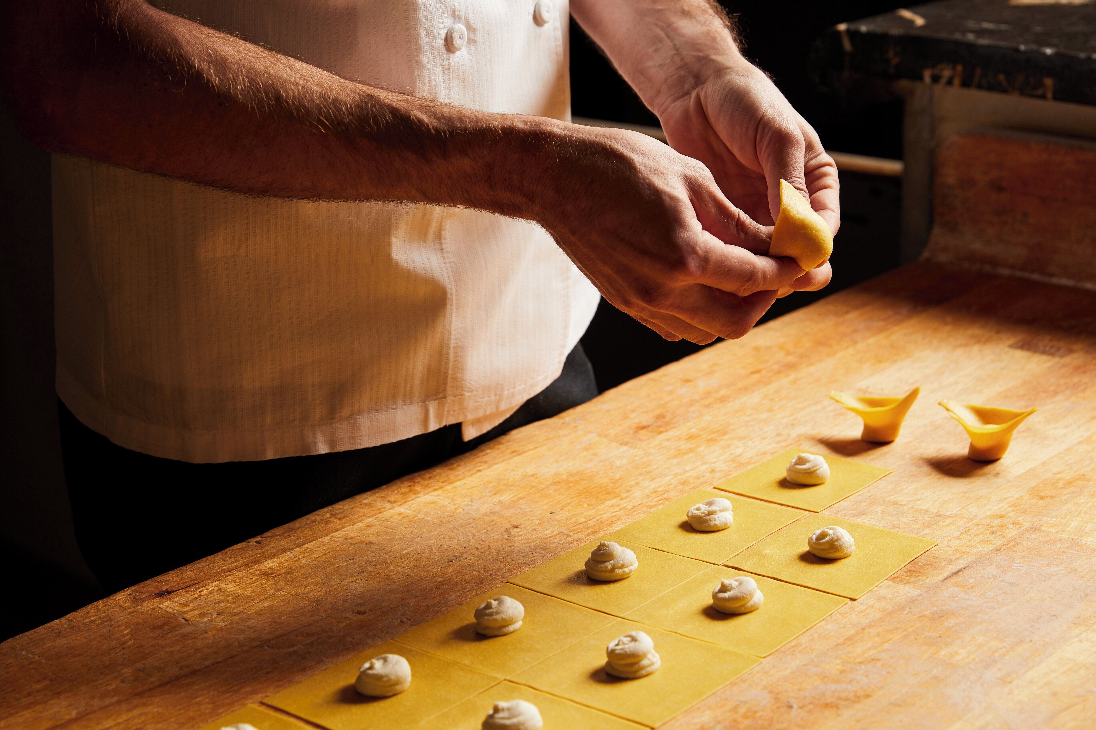 A person preparing food on a wooden table with dough balls and a yellow baking sheet.