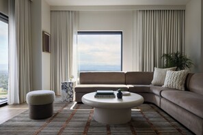 A modern living room with a beige sofa, a round coffee table, and a view of the cityscape through large windows. - Kimpton Claret Hotel by IHG (Denver)