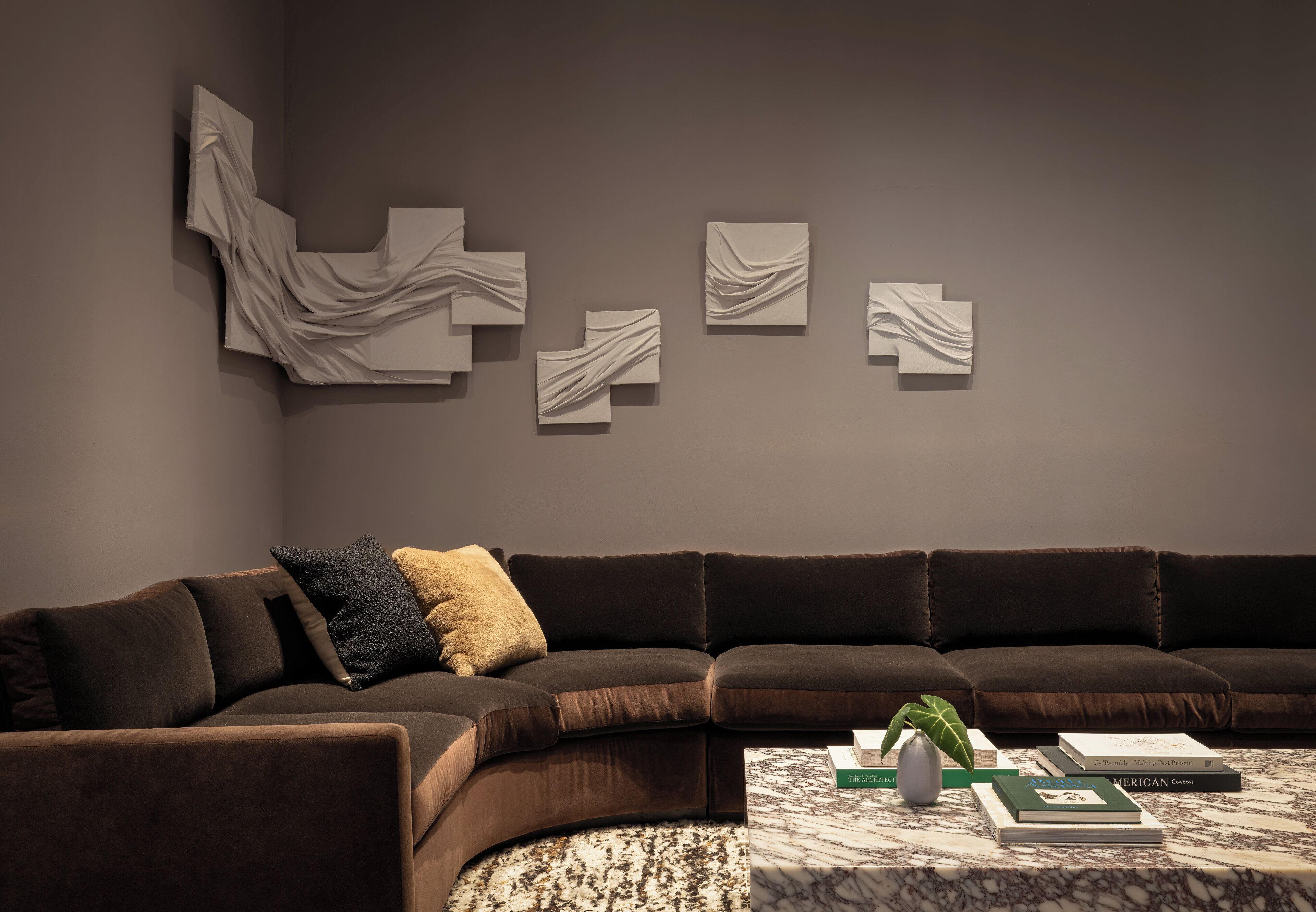 A modern living room with a dark brown sectional sofa, a marble coffee table, and abstract wall art.