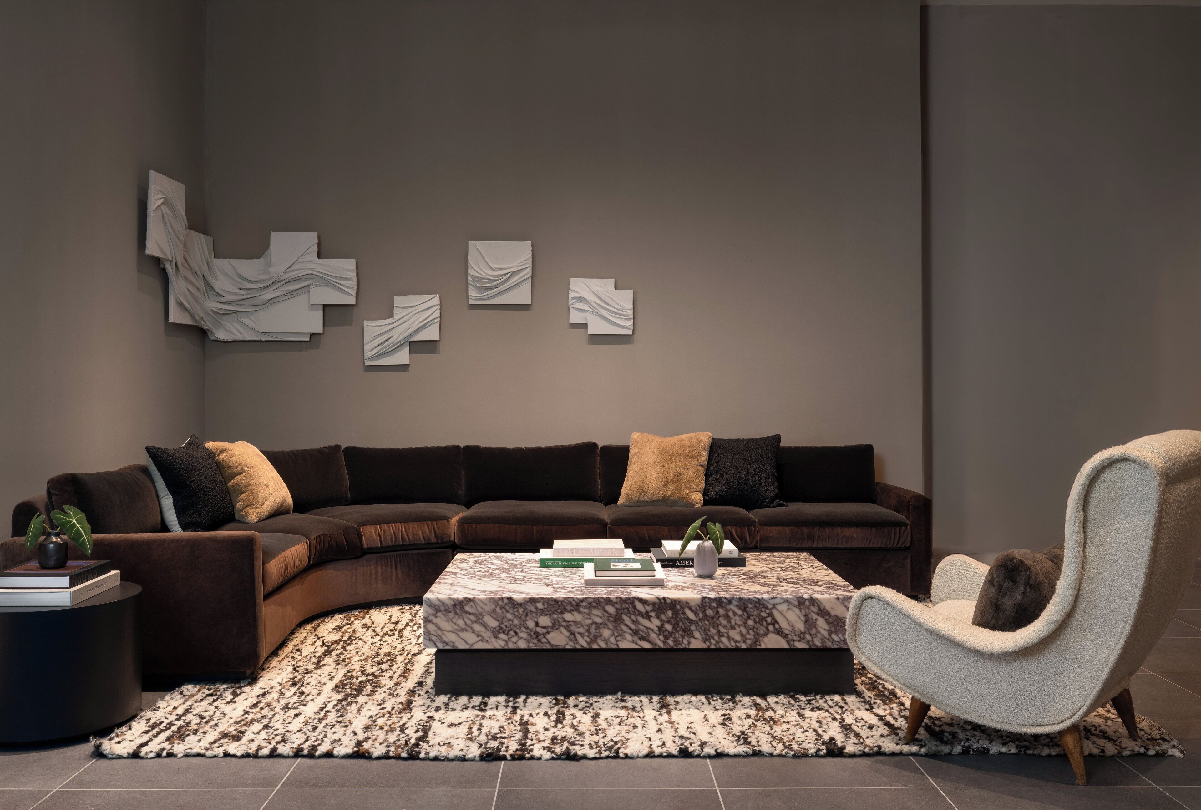 A modern living room with a dark brown sectional sofa, a marble coffee table, and a fluffy armchair.