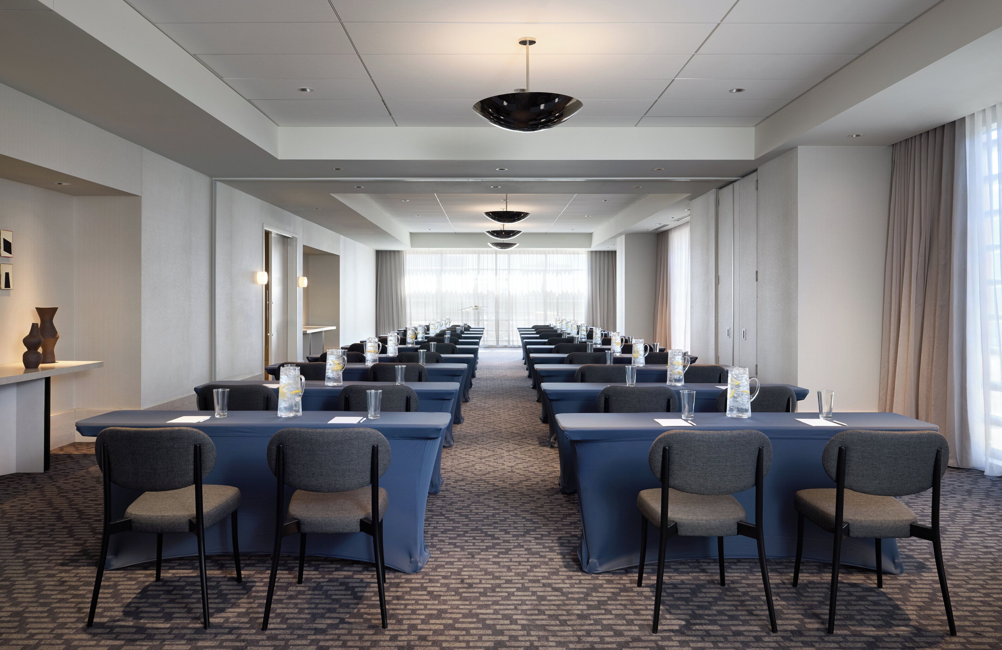 A conference room with long tables and chairs, a patterned carpet, and a large window with curtains.