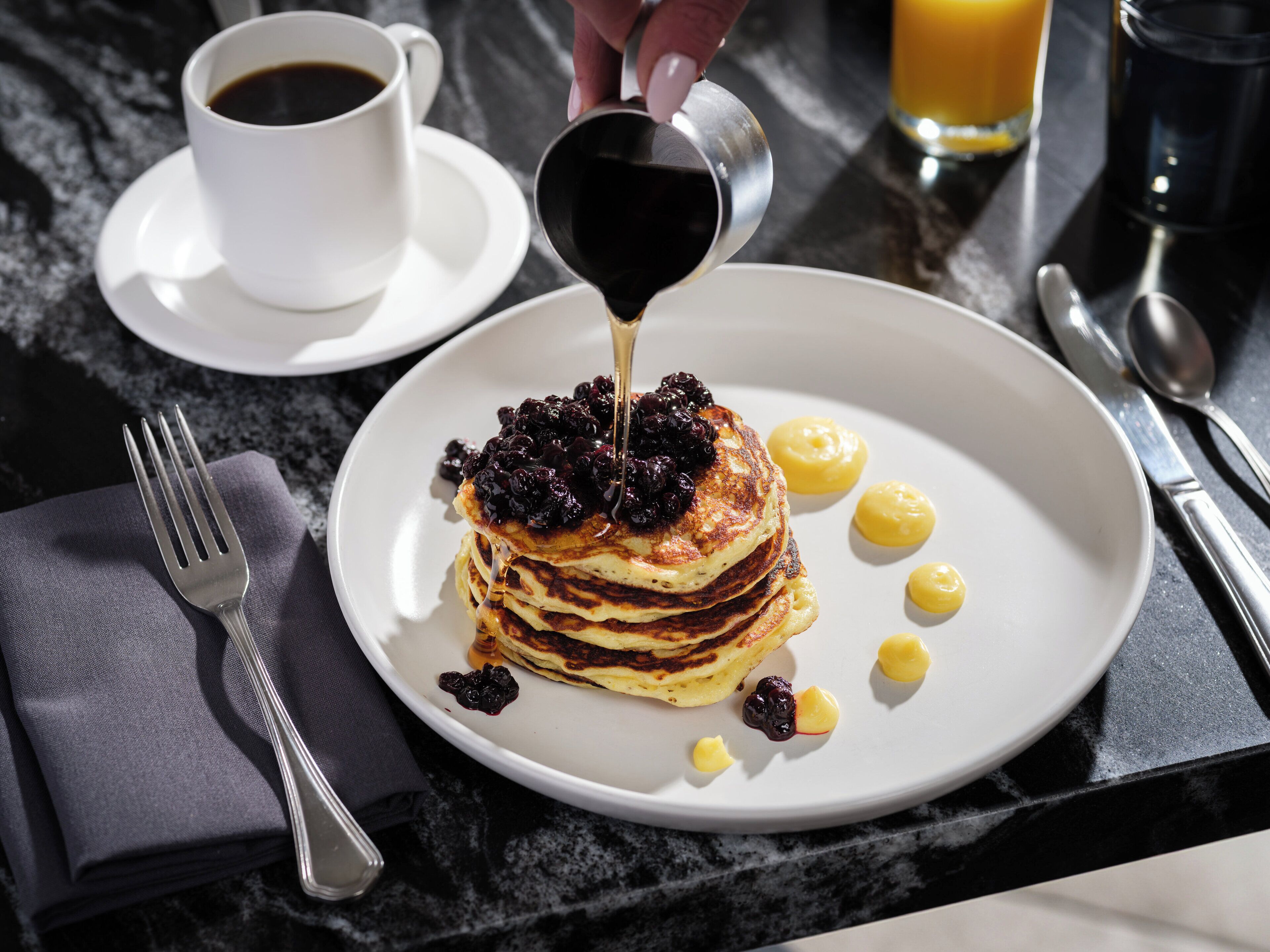 A breakfast plate with pancakes, syrup, and fruit on a table.