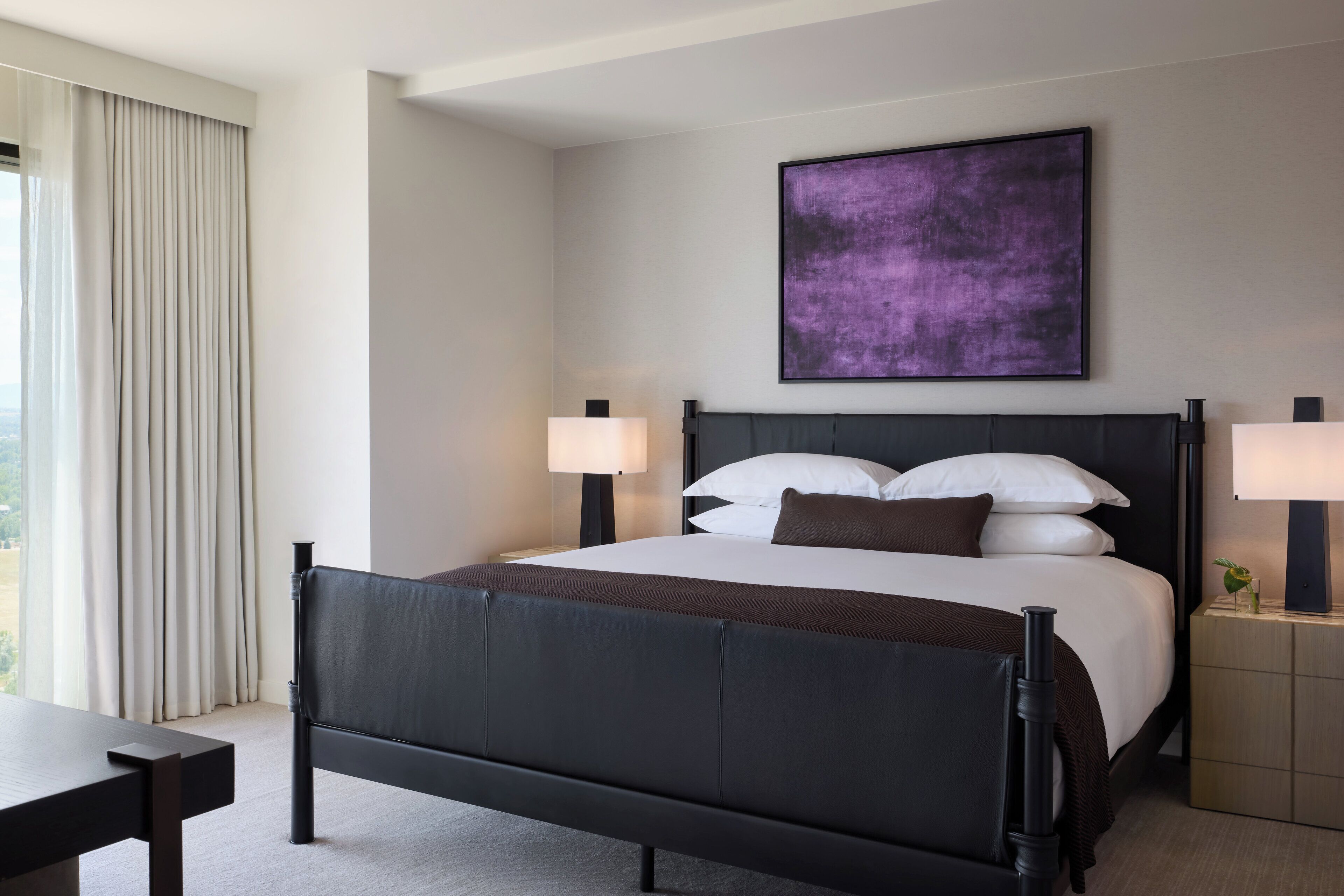 A modern hotel room with a large bed, two bedside tables, a nightstand, and a window with curtains.