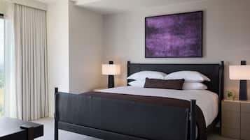 Una habitación de hotel moderna con una cama grande, dos mesitas de noche y un ventanal con cortinas.