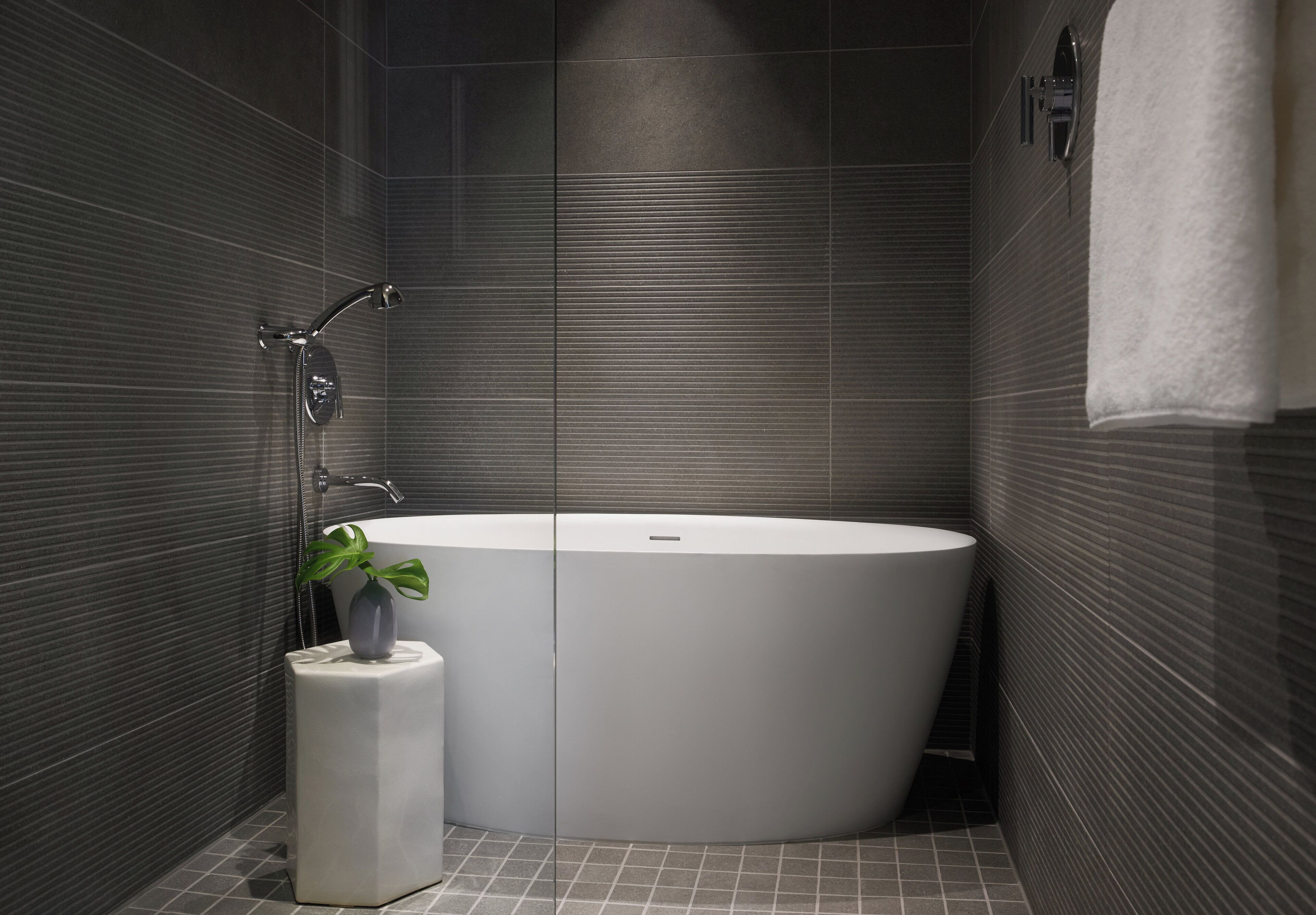 A modern bathroom with a freestanding bathtub, a small plant, and a towel rack.