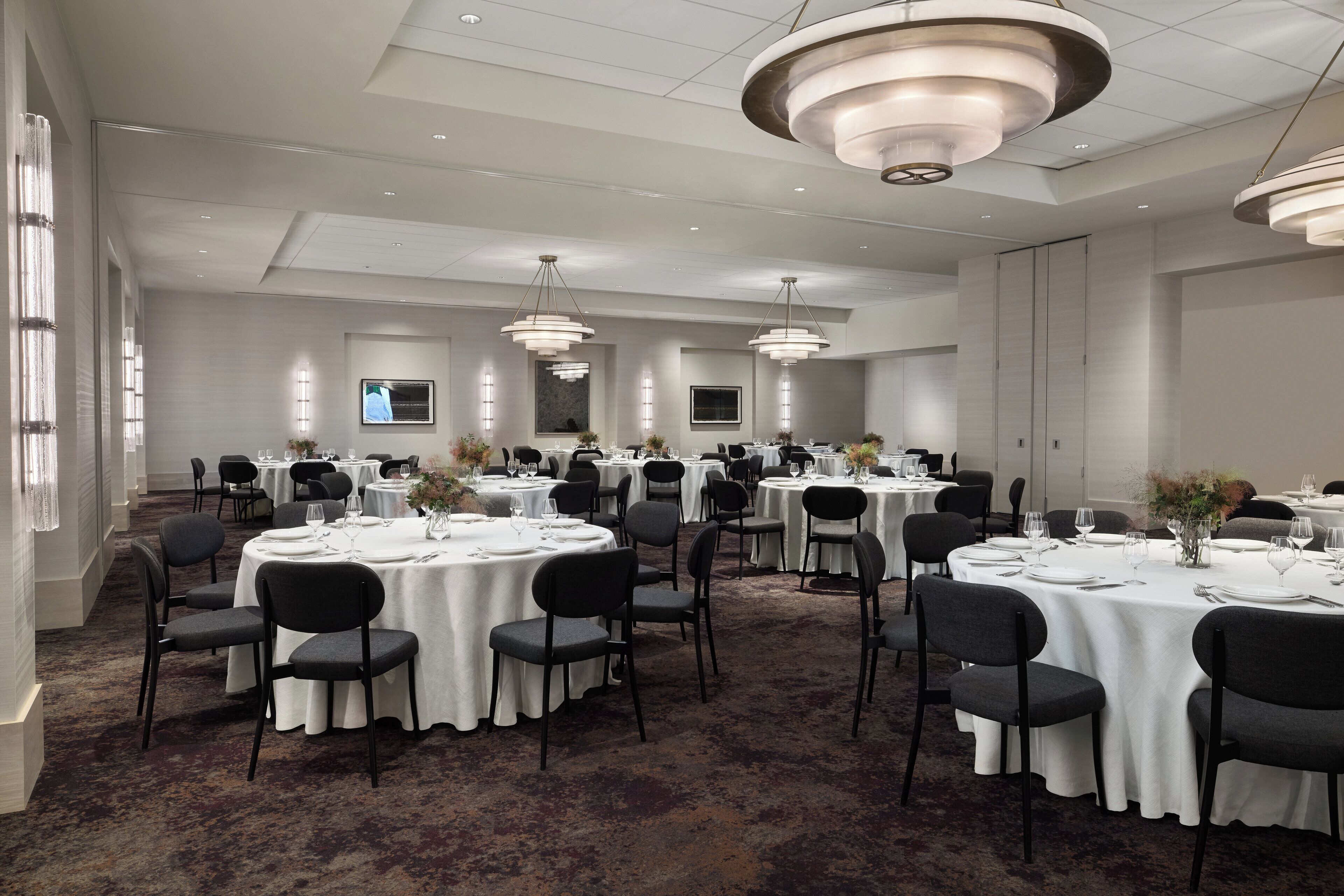 A spacious banquet hall with round tables, black chairs, and white tablecloths.