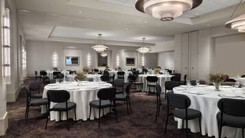 A spacious banquet hall with round tables, black chairs, and white tablecloths.