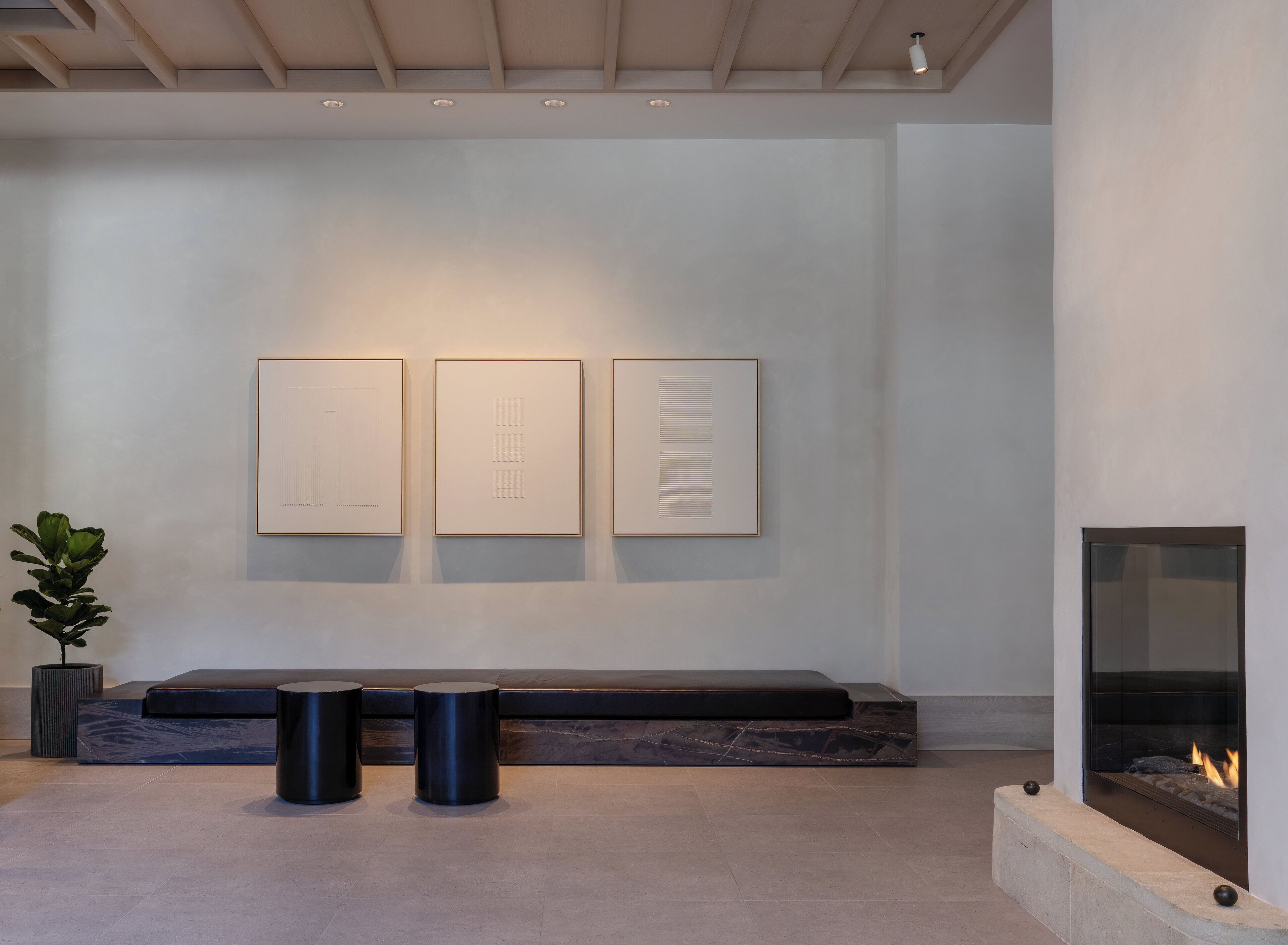 A modern interior with a fireplace, a bench, and three framed artworks on the wall.