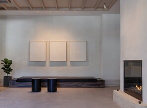 A modern interior with a fireplace, a bench, and three framed artworks on the wall. - Kimpton Claret Hotel by IHG (Denver)