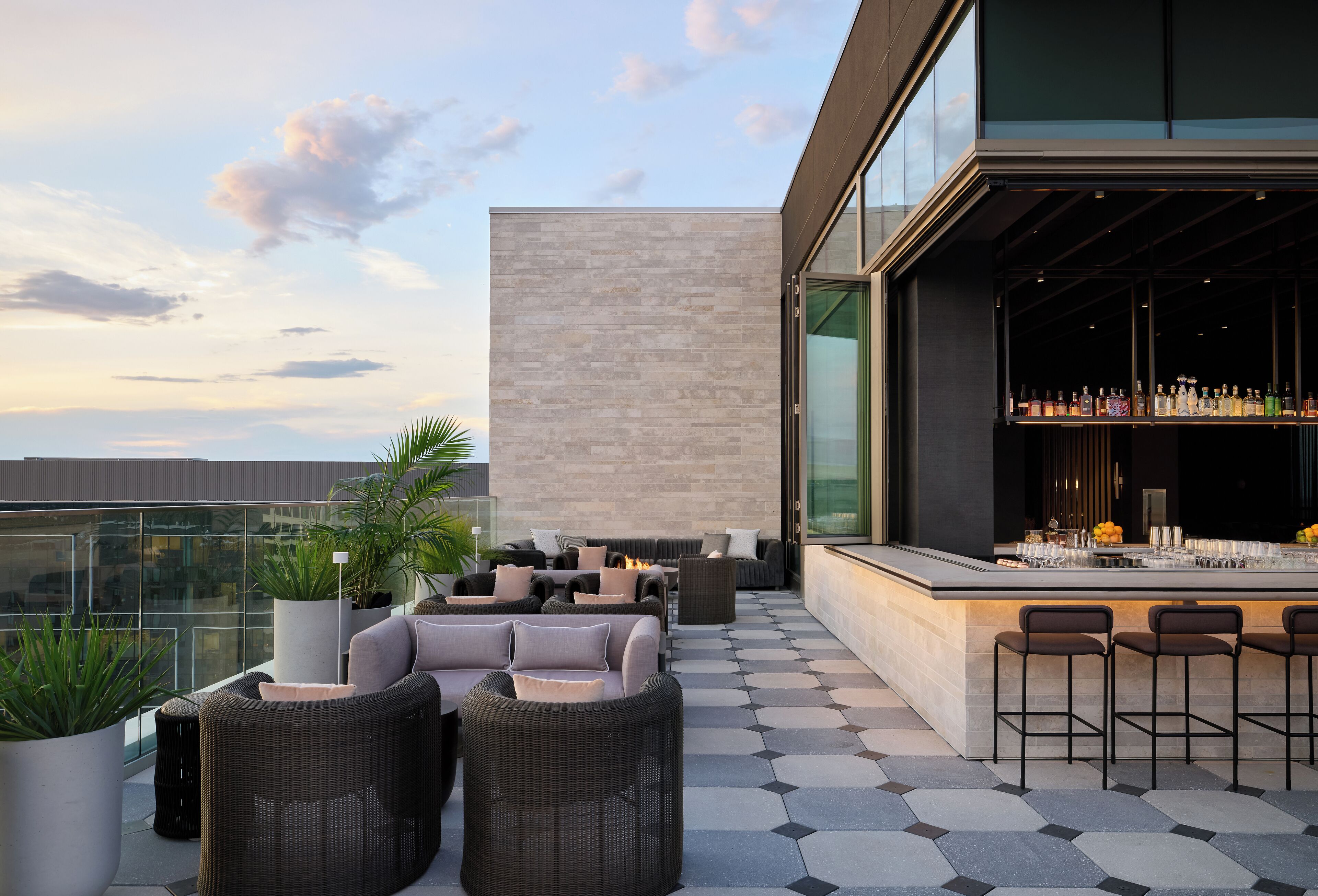 A rooftop bar with outdoor seating, a bar counter, and a large window overlooking the city.